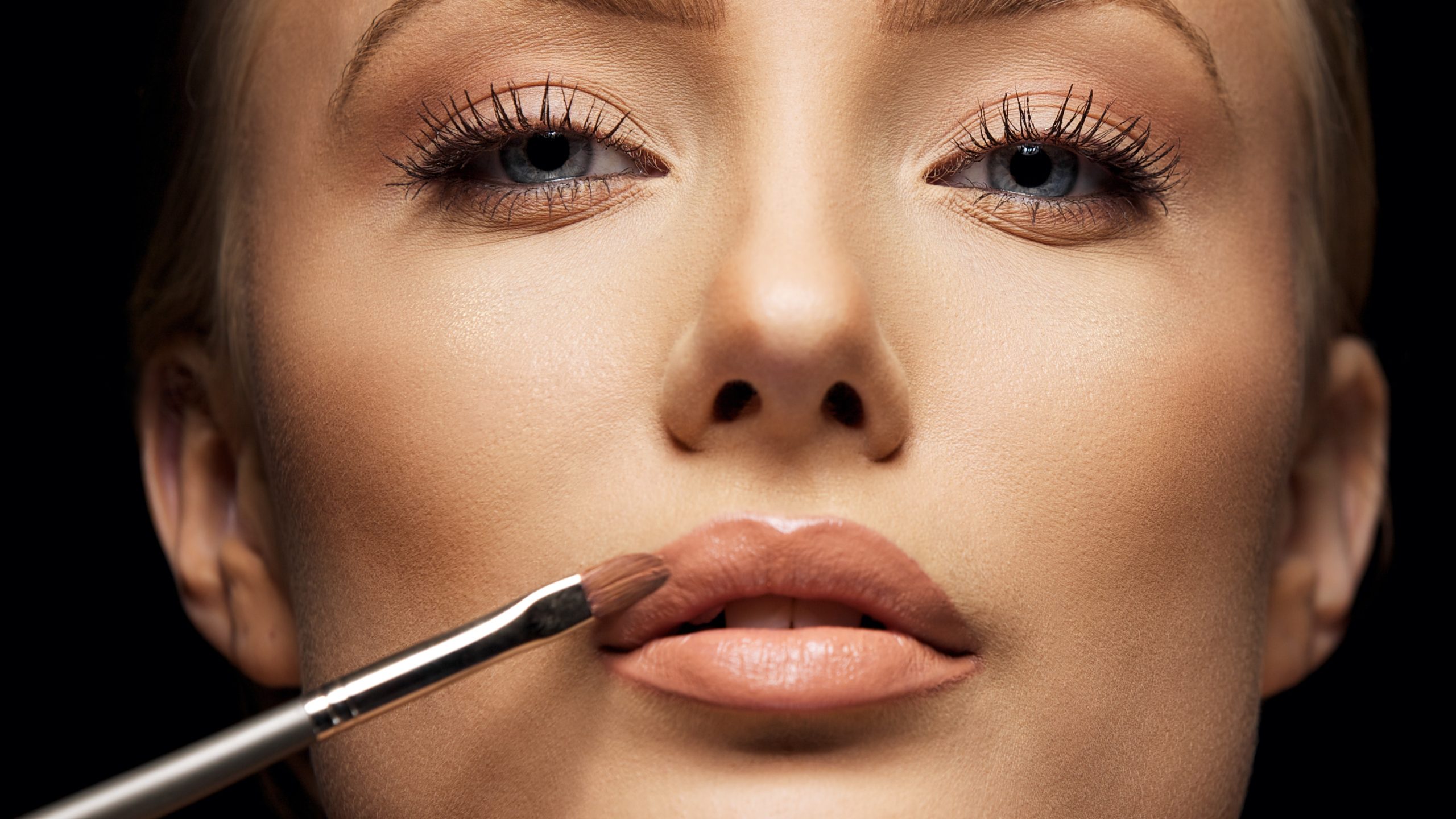 close up female face with makeup lipstick brush young woman applying lip gloss with make up brush on lips tight crop BpbUHNUNtx scaled