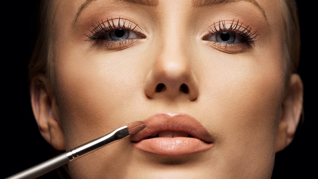 close up female face with makeup lipstick brush young woman applying lip gloss with make up brush on lips tight crop BpbUHNUNtx